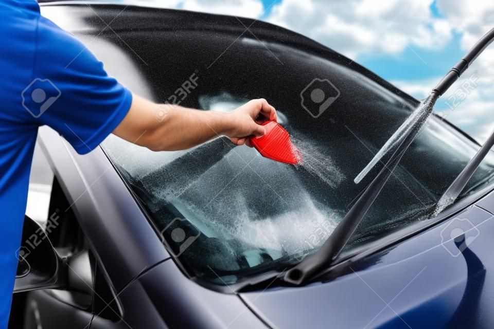 El hombre lava el parabrisas del coche.