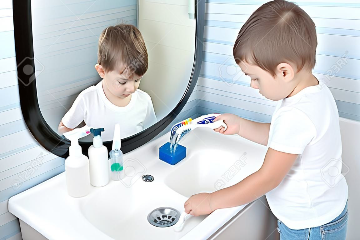 cute small child in white T-shirt washing his toothbrush under stream of water in bathroom