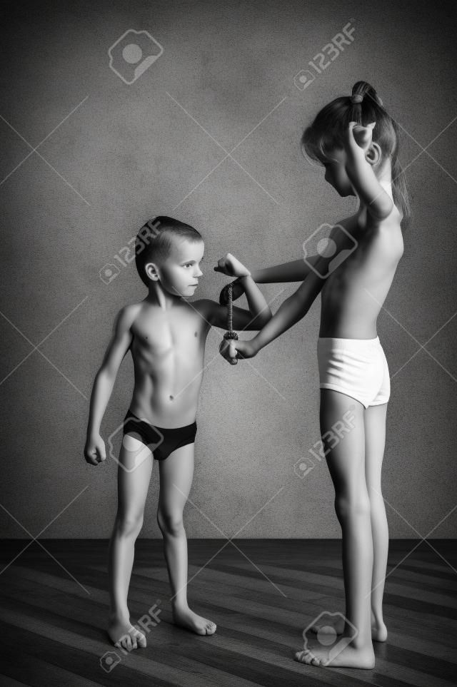 slim healthy caucasian little girl examines strong small boy muscle with measuring tape black and white photo