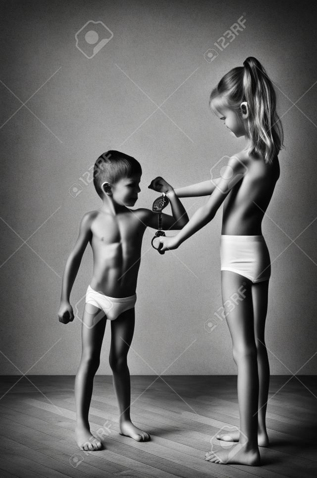 Karcsú, egészséges kaukázusi kislány erős kisfiú izomzatot mérőszalaggal fekete-fehér fotóval vizsgál