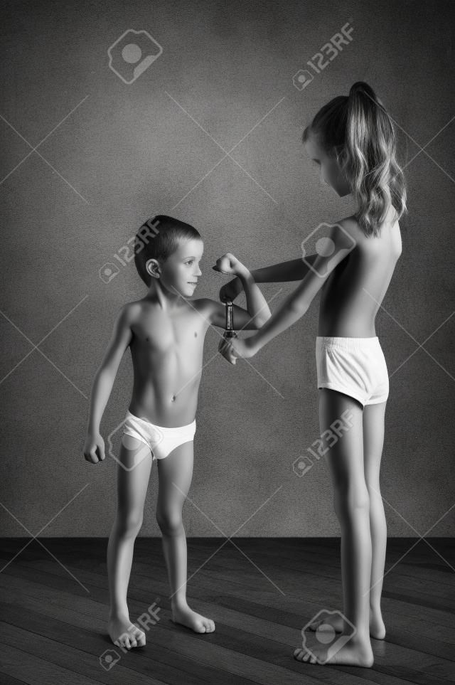 стройная здоровая кавказская маленькая девочка изучает крепкие маленькие мышцы мальчика с рулеткой черно-белое фото