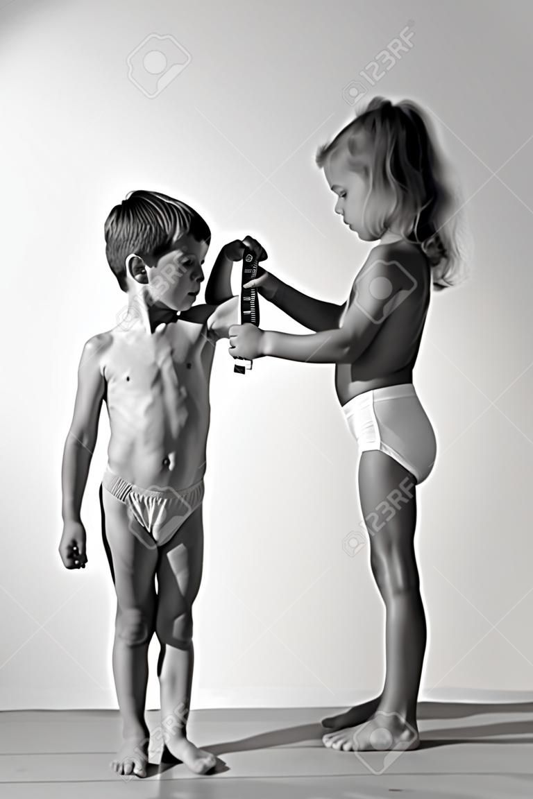 slim healthy caucasian little girl examines strong small boy muscle with measuring tape black and white photo