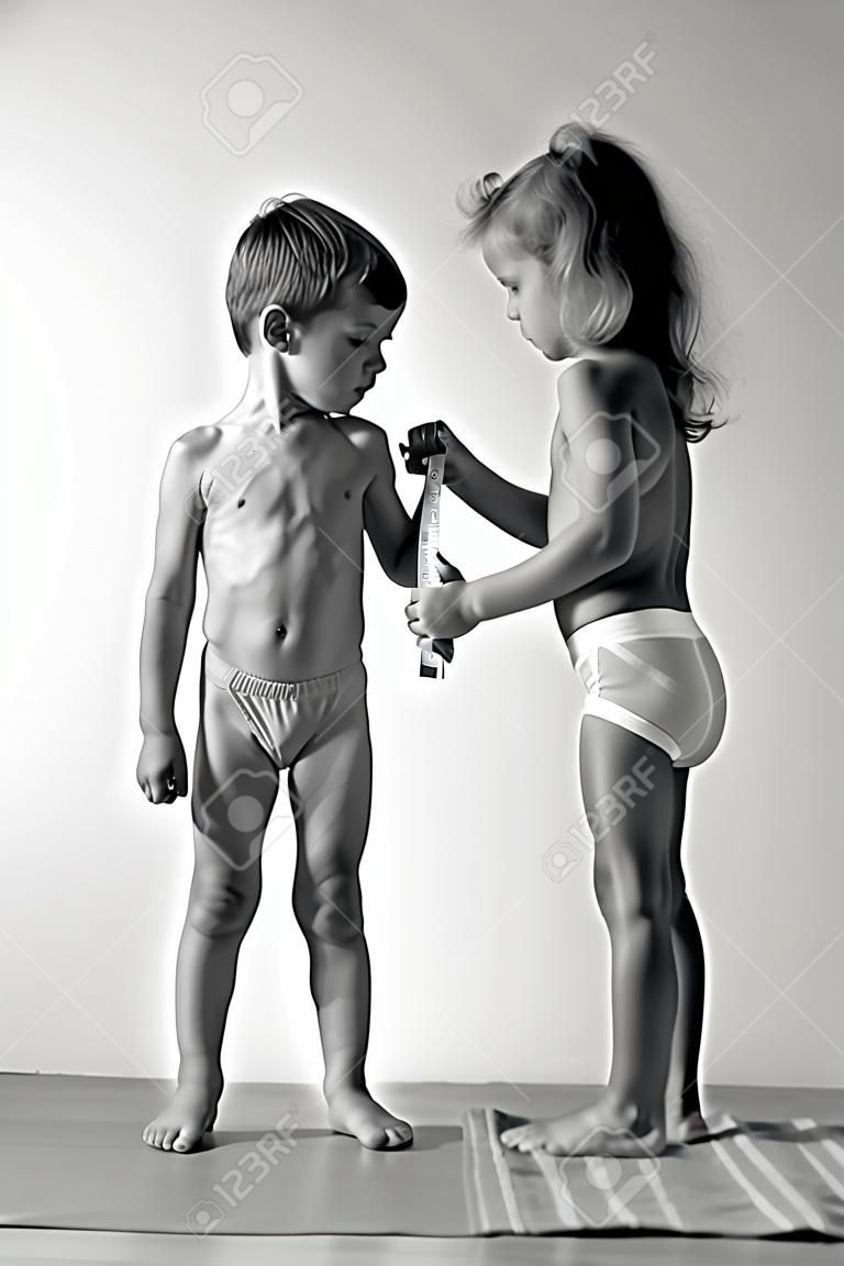 стройная здоровая кавказская маленькая девочка изучает крепкие маленькие мышцы мальчика с рулеткой черно-белое фото