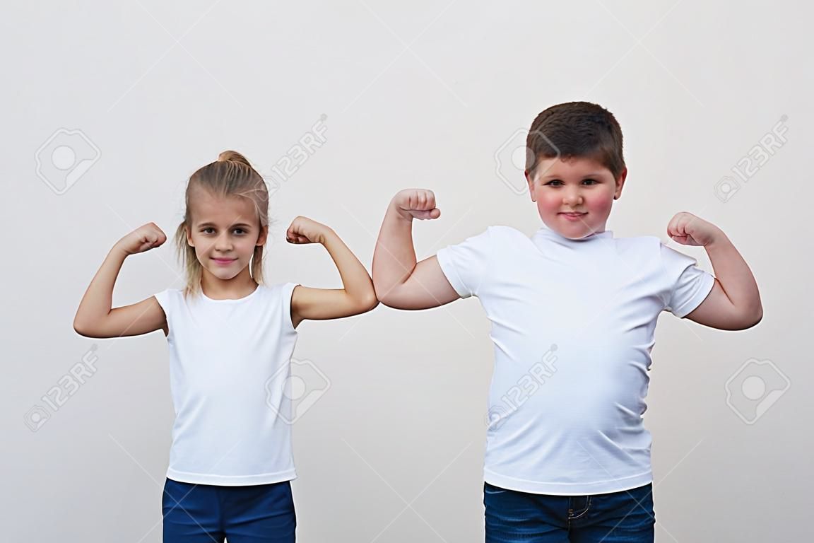 two children little thin girl and thick boy showing their muscle on copyspace background
