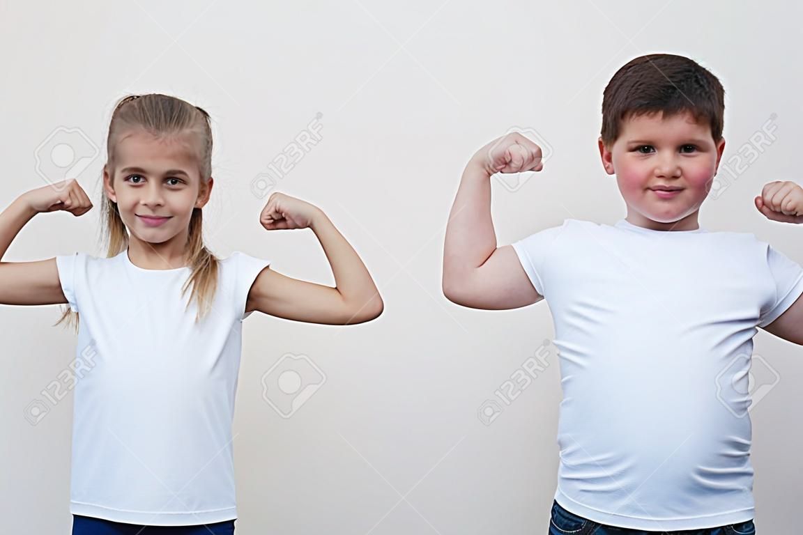 two children little thin girl and thick boy showing their muscle on copyspace background