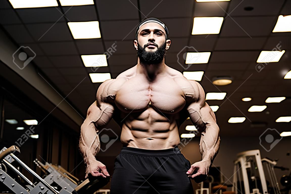 Młody brodaty sportowiec z silnymi mięśniami w ciemnej siłowni w klubie fitness