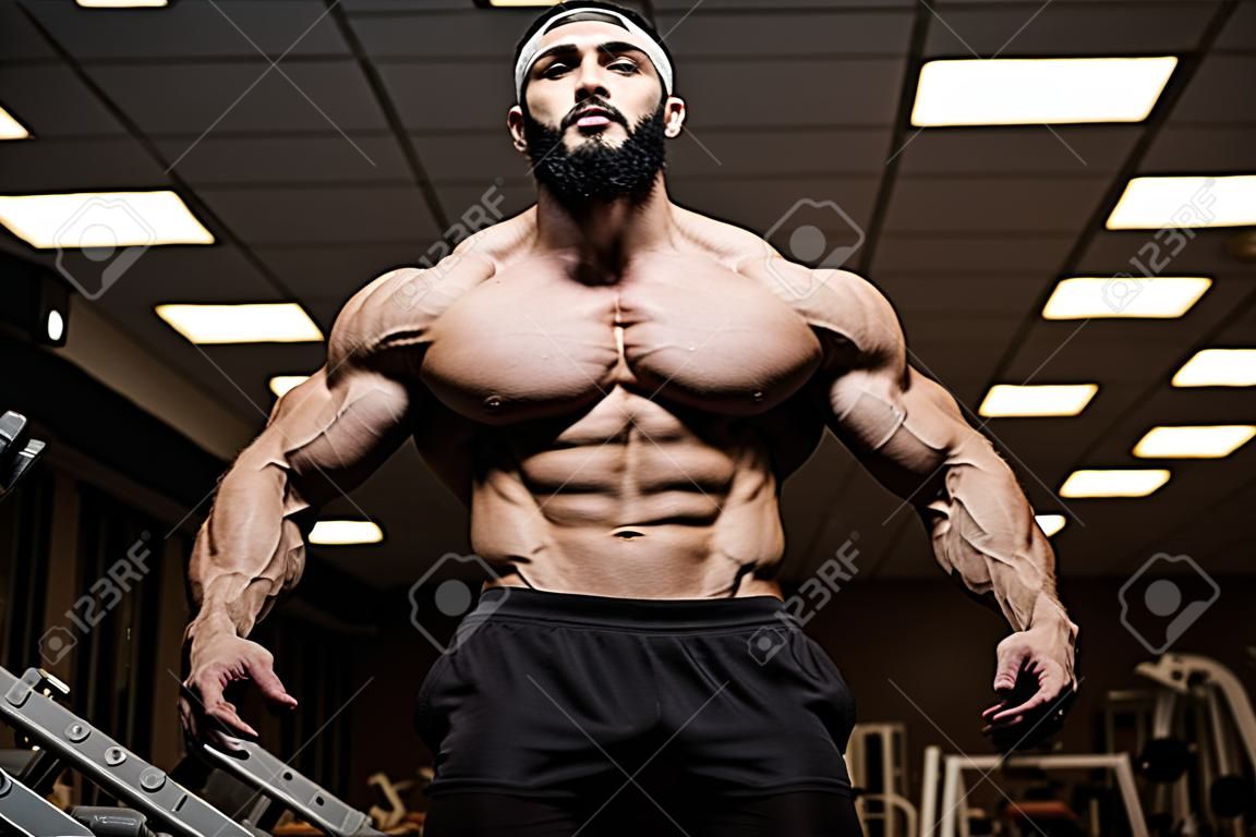young bearded athlete with strong muscles in dark fitness club gym
