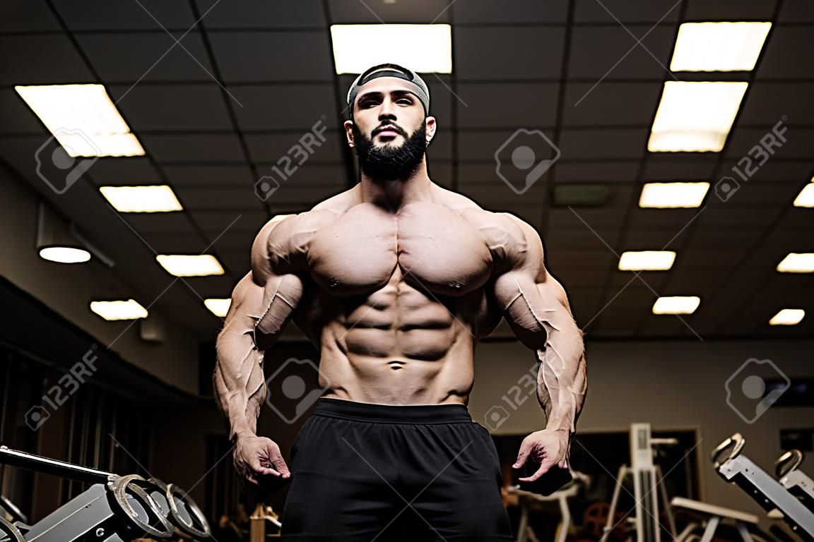 Młody brodaty sportowiec z silnymi mięśniami w ciemnej siłowni w klubie fitness