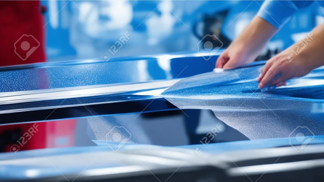 The protective film is removed from the machine with a paper knife. Car wrapping specialists straightening vinyl foil or film to remove ari bubbles cut carbon film