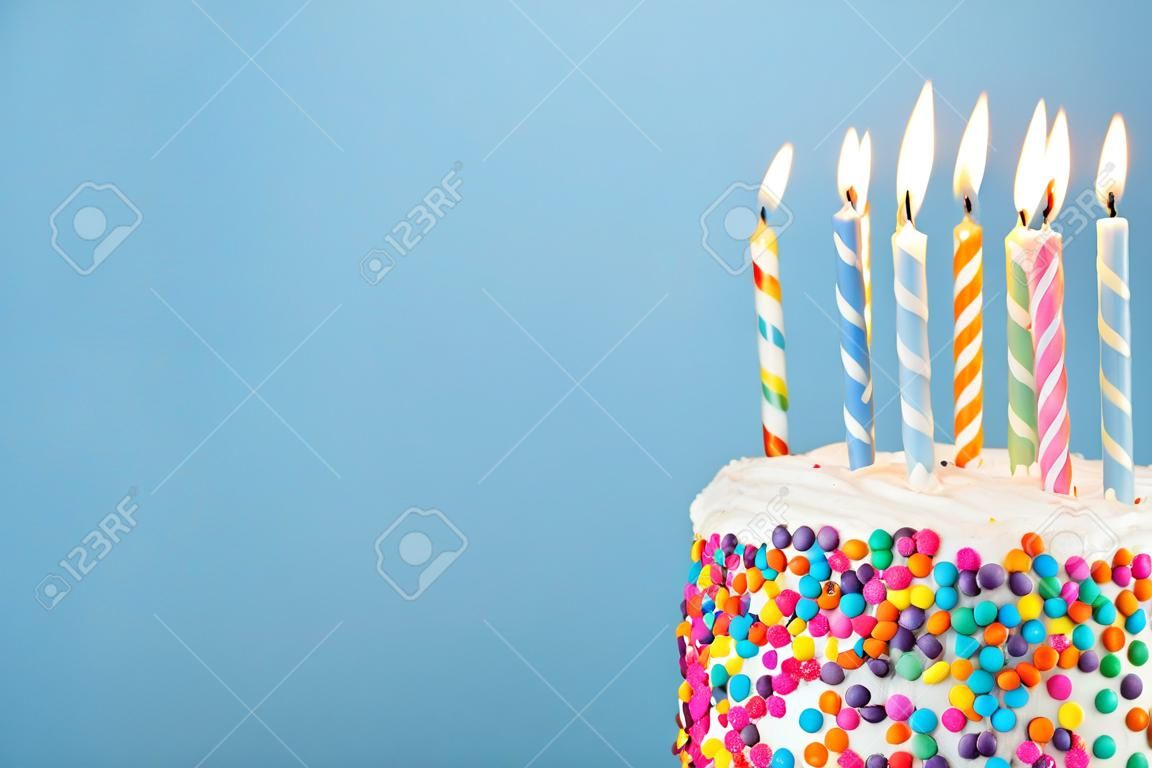Tort urodzinowy z mnóstwem kolorowych świeczek i posypką na niebieskim tle