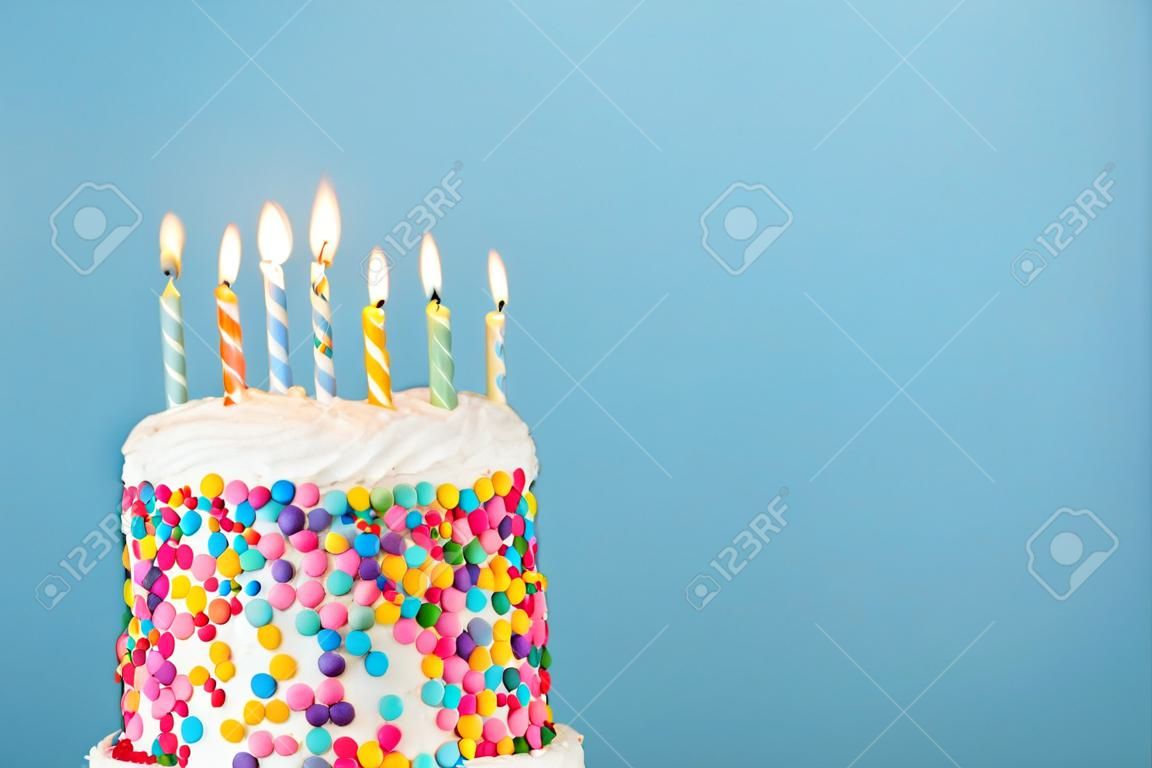 Verjaardagstaart met veel kleurrijke kaarsen en bestrooiingen op een blauwe achtergrond
