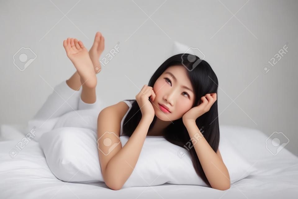 Pensar cara de la mujer de cerca mientras está acostado en la cama en su casa, aislados en fondo blanco, modelo es una chica asiática