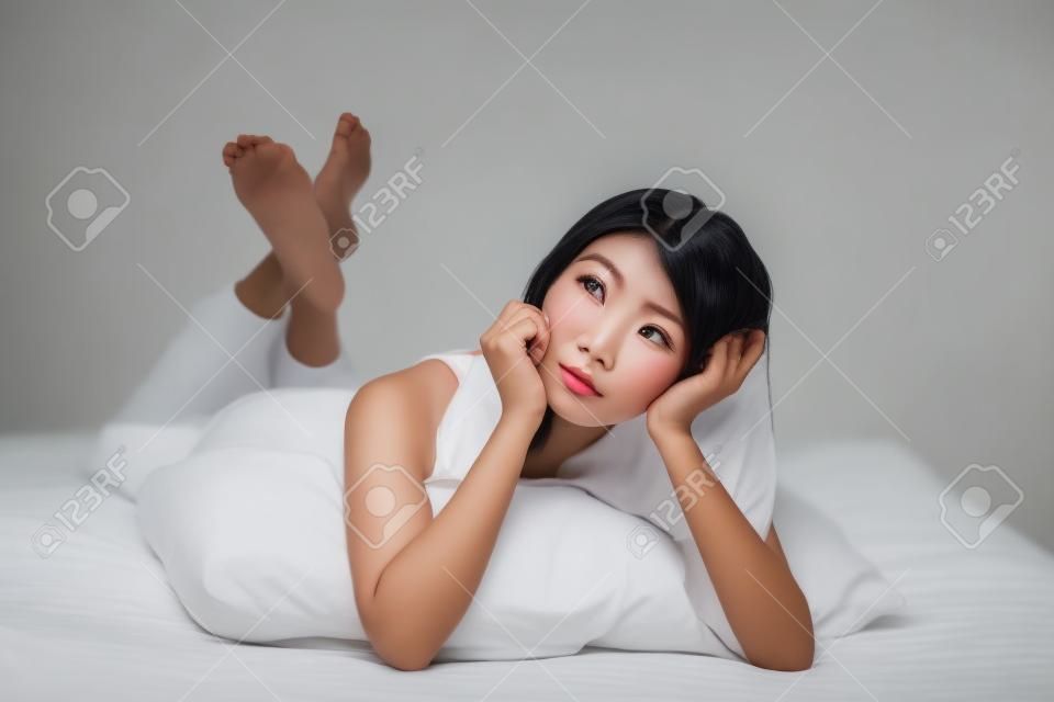 Penser visage de femme près en étant couché sur le lit à la maison, isolée sur fond blanc, le modèle est une jeune fille asiatique
