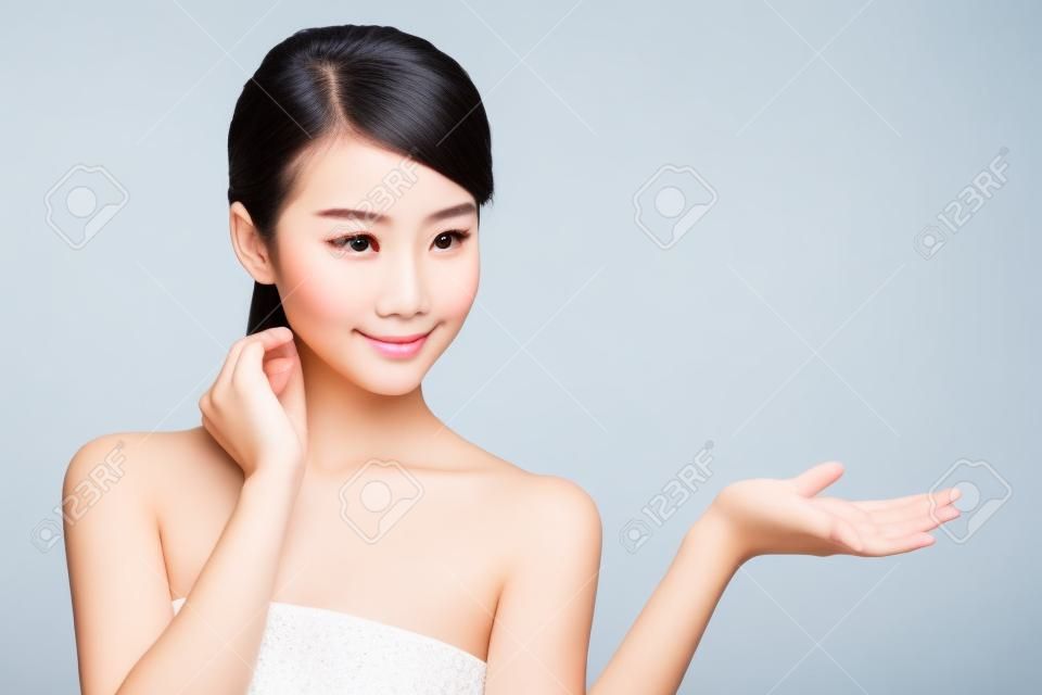 건강한 깨끗한 피부는 그녀의 손에 뭔가 제시와 함께 아름 다운 젊은 여자. 흰색에 격리. 아시아 아름다움