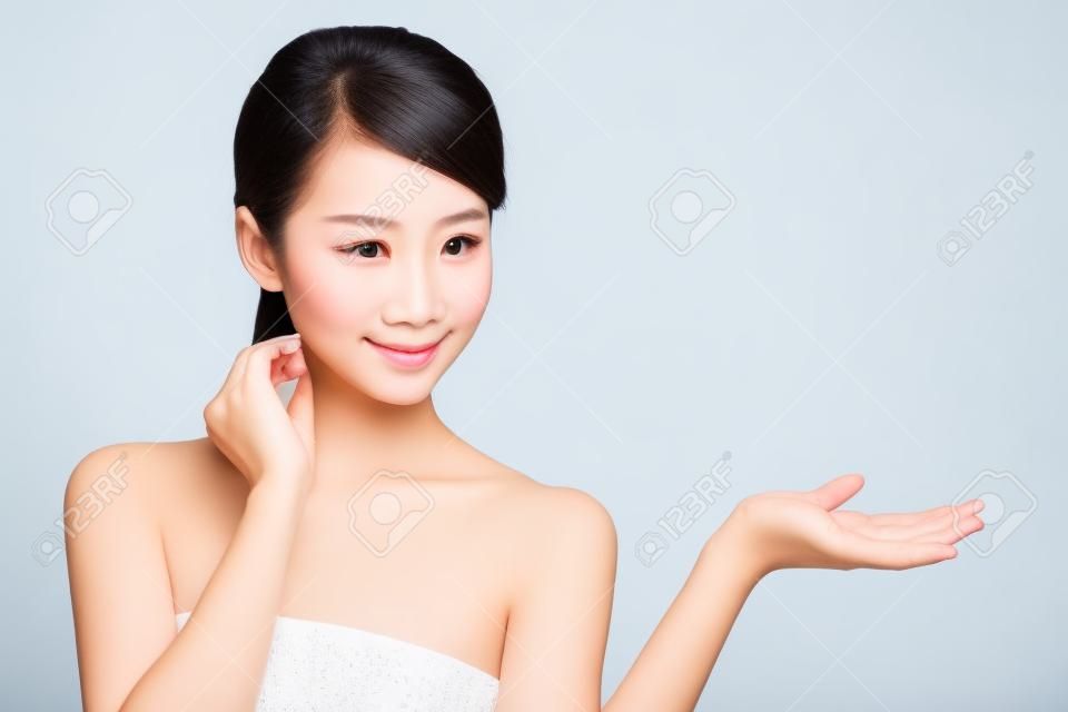 Gyönyörű fiatal nő egészséges, tiszta bőr megmutat valamit a kezét. Elszigetelt fehér. ázsiai szépség