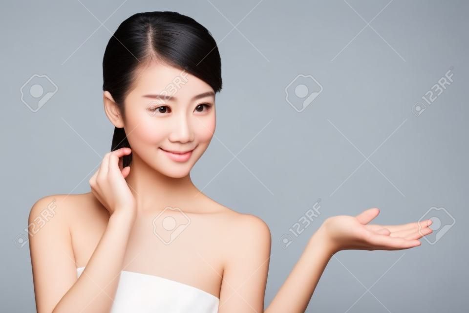 Gyönyörű fiatal nő egészséges, tiszta bőr megmutat valamit a kezét. Elszigetelt fehér. ázsiai szépség