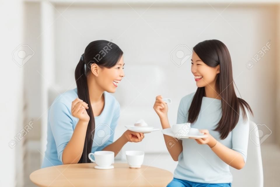 兩個幸福的年輕女性朋友咖啡杯和蛋糕享受在客廳在家中談話，健康生活方式的理念，亞洲美容