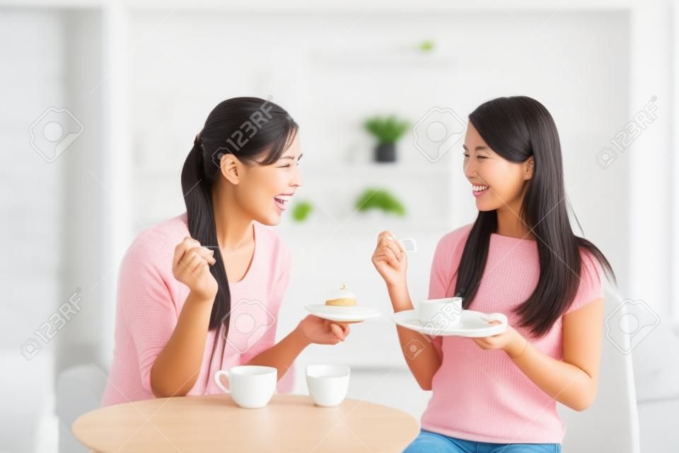 Due giovani amici femminili con tazze di caffè e torte godendo di una conversazione in salotto a casa, sano concetto di stile di vita, asiatico bellezza