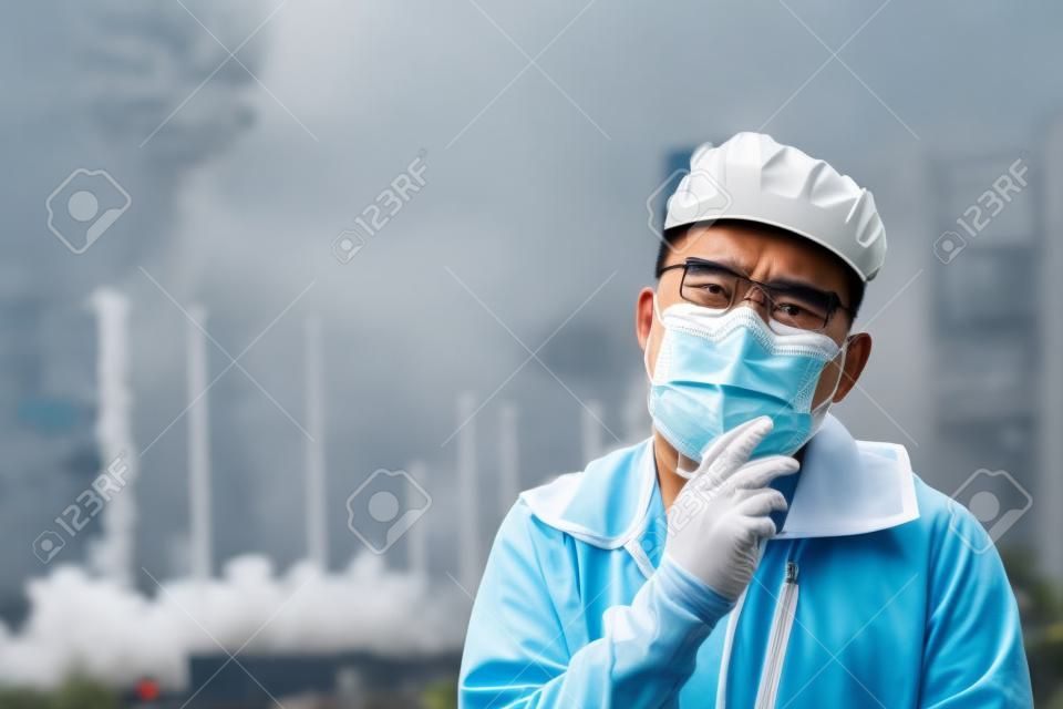 Aziatische man hoest en draagt beschermende n95 masker omdat luchtverontreiniging voor de fabriek