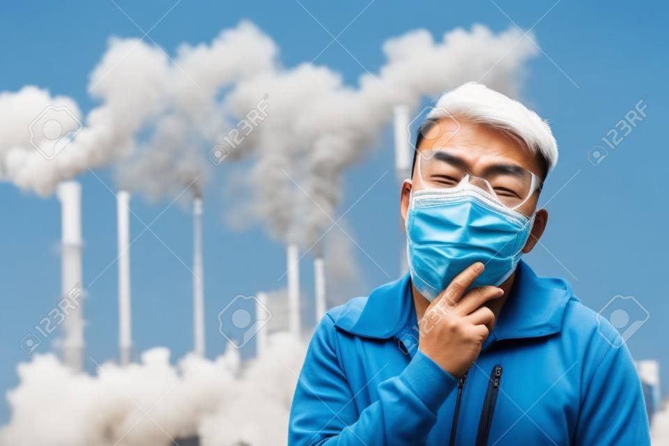 Aziatische man hoest en draagt beschermende n95 masker omdat luchtverontreiniging voor de fabriek
