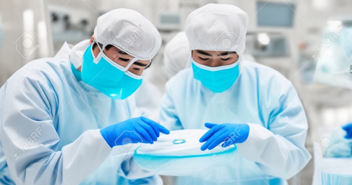 滅菌カバーオールの2人のアジア人技術者が、さまざまな色を反射する手袋でウェーハを保持し、半導体製造工場でチェックします