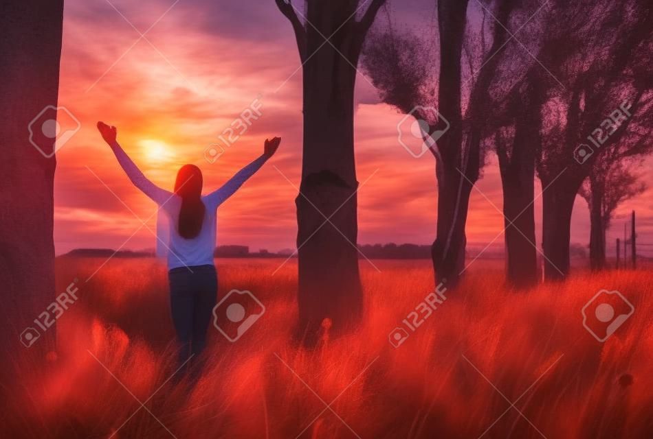 Mujer joven que se siente victoriosa frente a la hermosa puesta de sol.