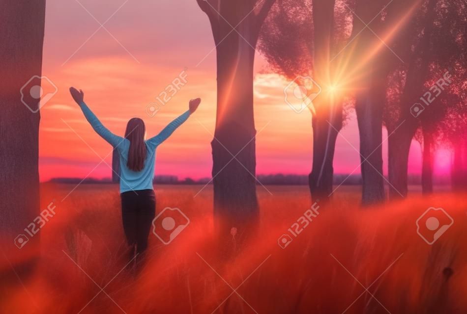 Mujer joven que se siente victoriosa frente a la hermosa puesta de sol.