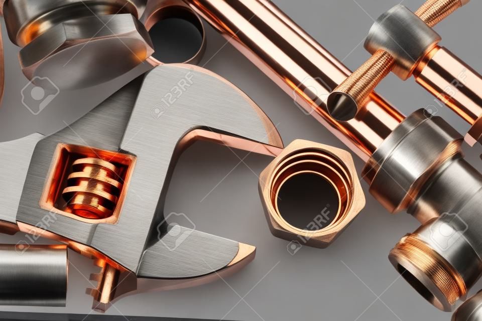 Nuevas tuberías de cobre listas para la construcción - Llave ajustable, tubería de cobre de 15 mm y juntas de latón colocadas juntas contra un fondo gris