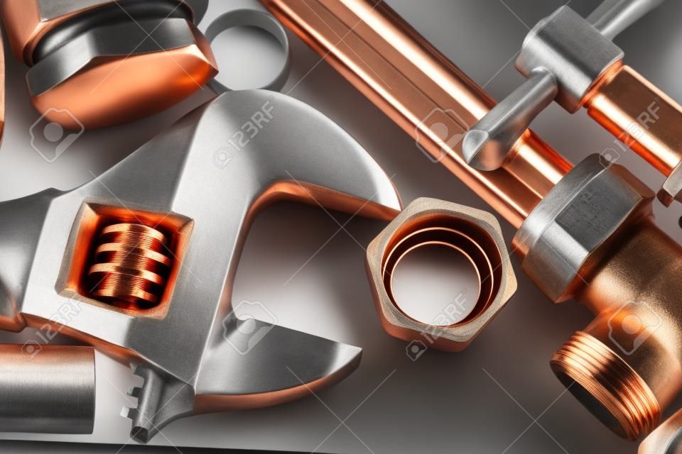 Новые медные трубы готовы к строительству - Регулируемый ключ, 15 мм медный трубопровод и латунные соединения, сложенные на сером фоне