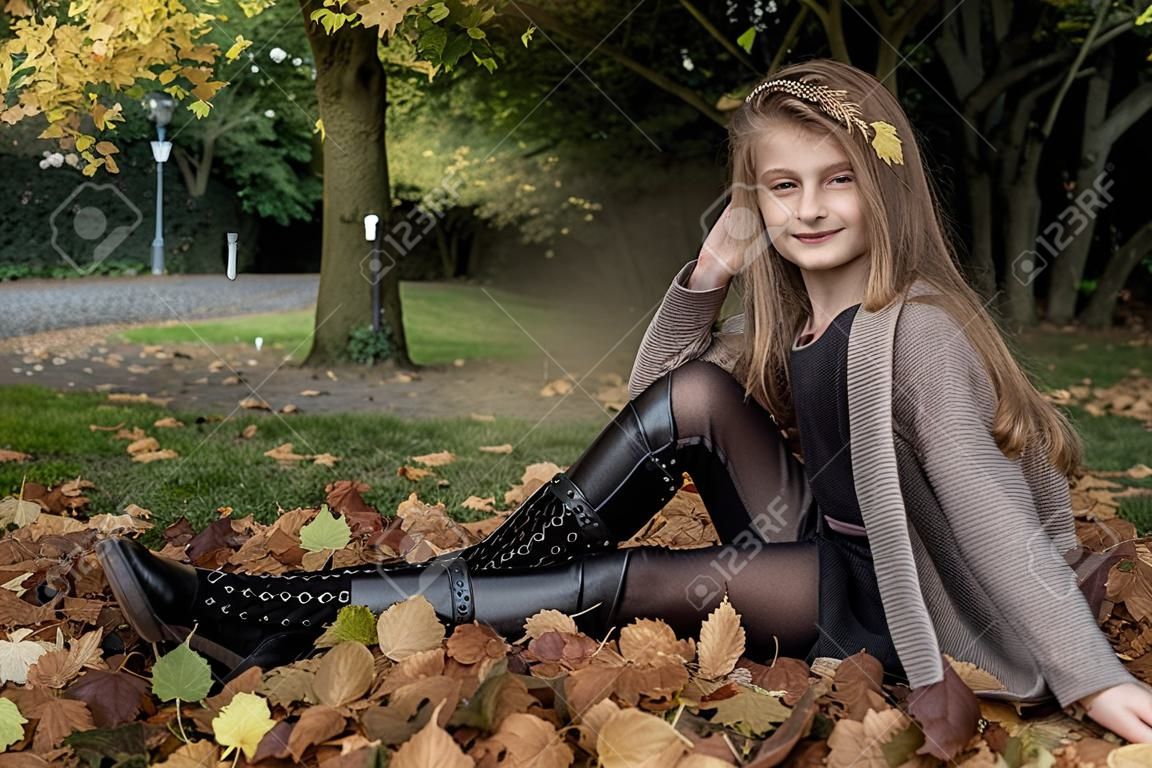 Kindermode. Schönes junges kleines Mädchen im Herbstwinteroutfit über Herbstlaubhintergrund im Park, im Freien. Kinderkleidung.