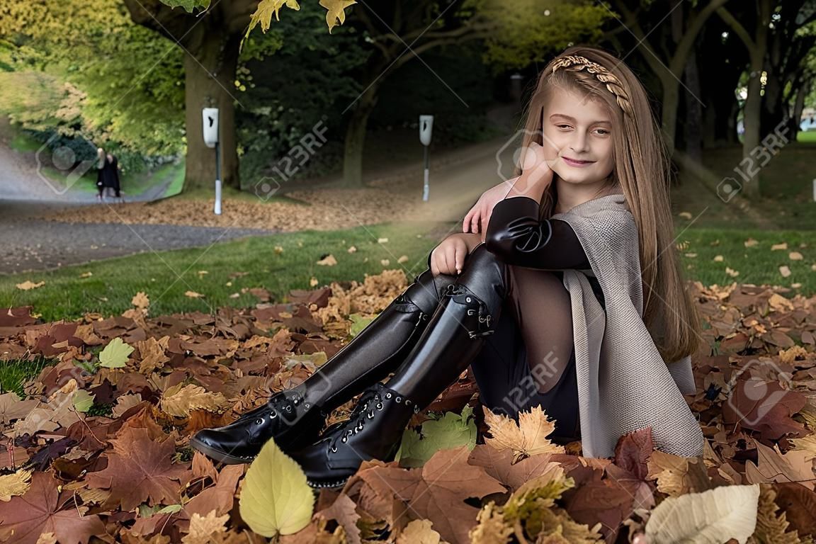 Moda infantil. Hermosa joven niña en traje de otoño invierno sobre fondo de hojas de otoño en el parque, al aire libre. Ropa de ninos.