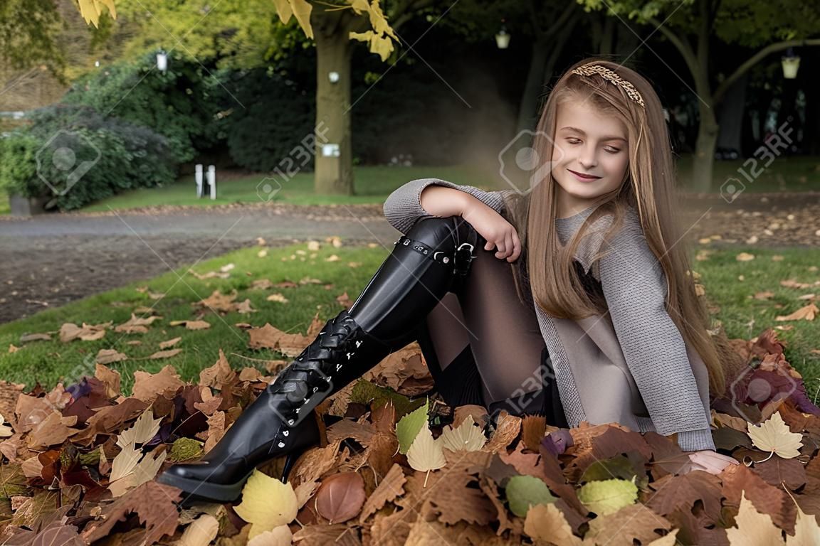 Moda infantil. Hermosa joven niña en traje de otoño invierno sobre fondo de hojas de otoño en el parque, al aire libre. Ropa de ninos.
