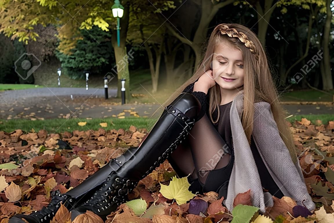 Kindermode. Schönes junges kleines Mädchen im Herbstwinteroutfit über Herbstlaubhintergrund im Park, im Freien. Kinderkleidung.