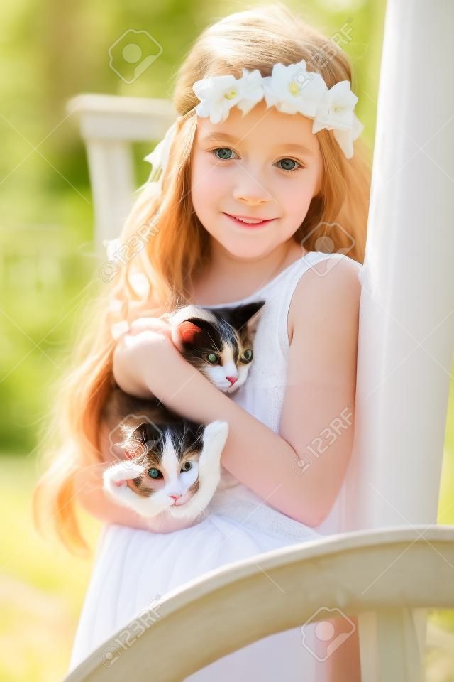 Portrait of a small cute child with tenderness and love a cat and smiles with happiness. Little girl relaxing on park with her kitten. Child in white communion dress is kissing a cat. Spring fashion