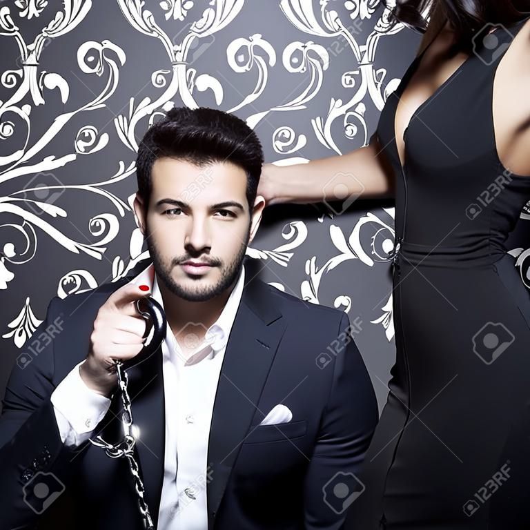 Macho rich businessman with lover holding handcuffs at vintage wall