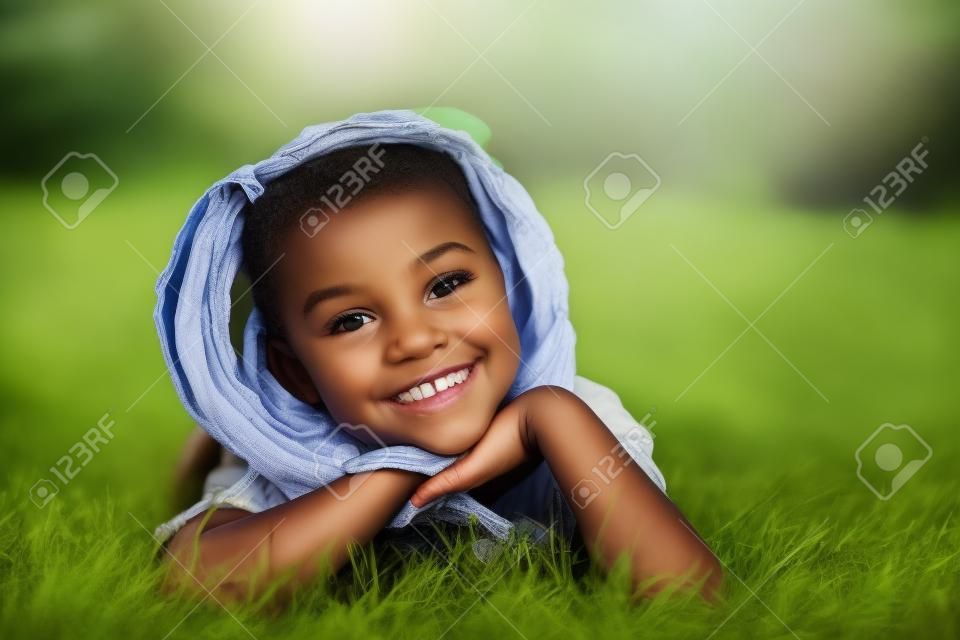 Outdoor ritratto di una giovane ragazza nera carina sdraiato sull'erba e sorridente - popolo africano