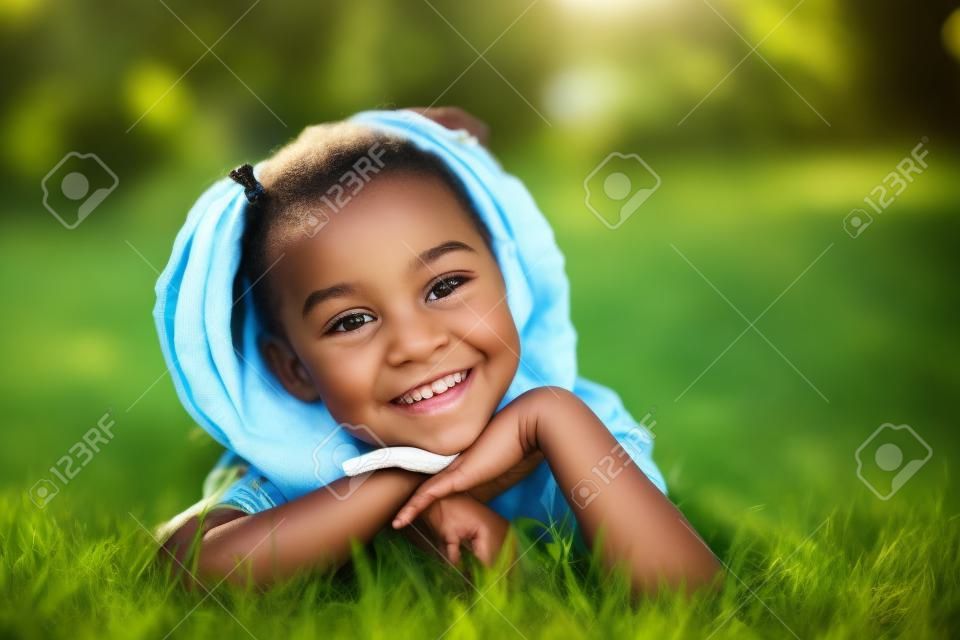 Outdoor ritratto di una giovane ragazza nera carina sdraiato sull'erba e sorridente - popolo africano