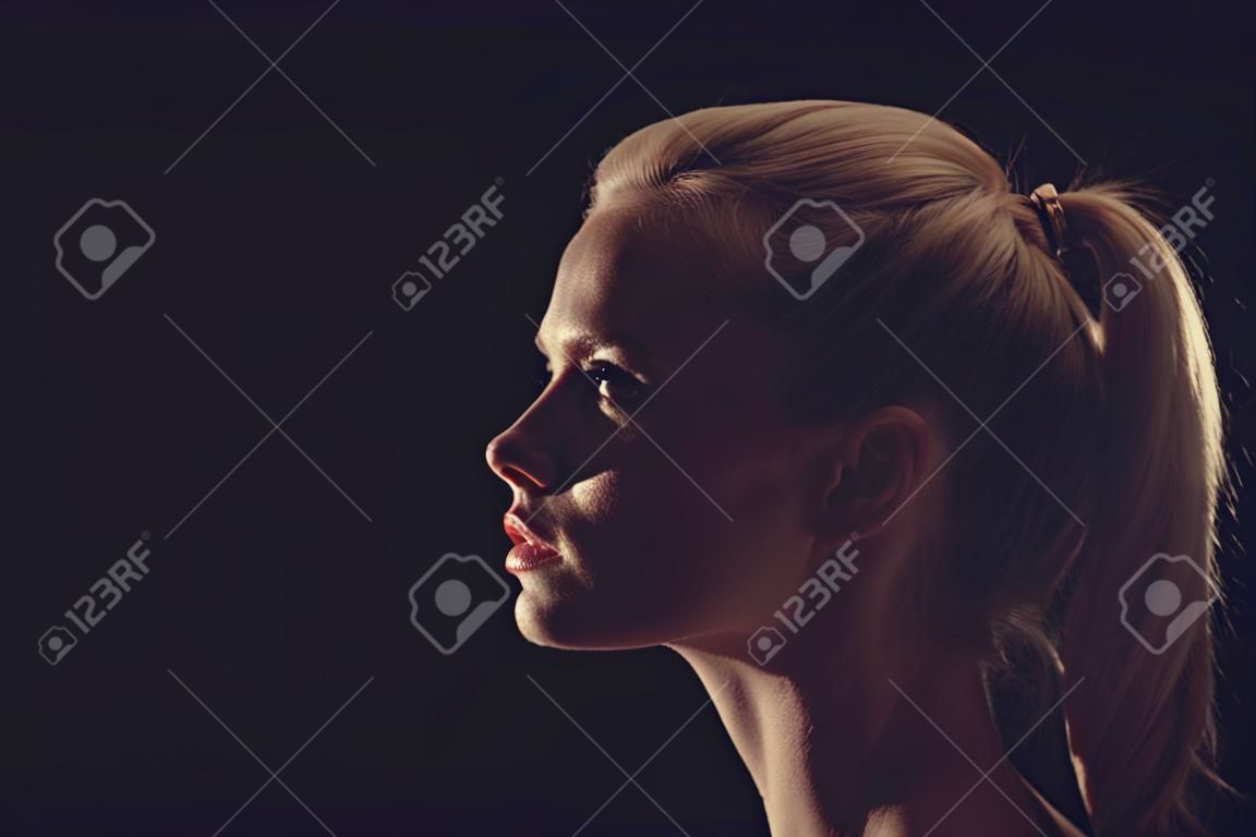 Portrait of beautiful blonde woman in darkness with soft light on her face, pensive silhuette in on black background.