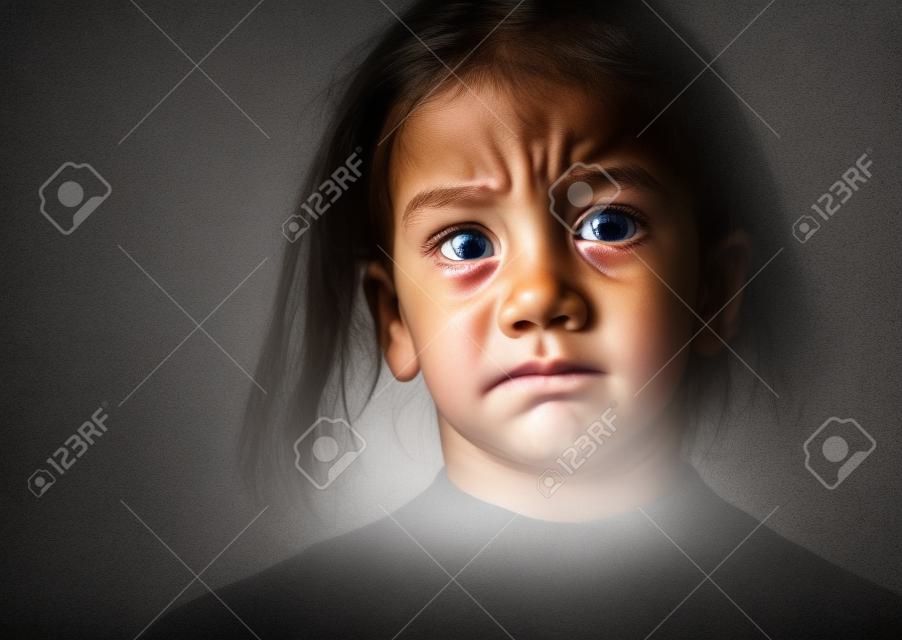 Closeup of a bullied, depressed, alone, tired, stressed young child girl crying. Isolated on black background. Human emotions, Childhood depression, emotional pain. Bullying and child abuse concept.