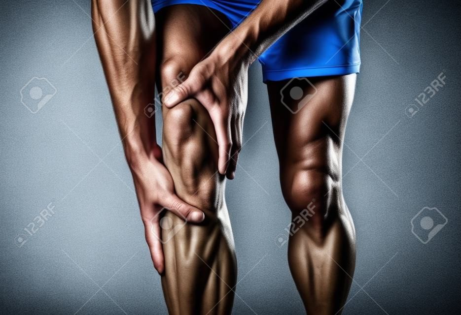 Young fit man holding knee with hands in pain after suffering muscle injury broken bone leg pain sprain or cramp during running workout. In Body pain and sport training injury and body health care.