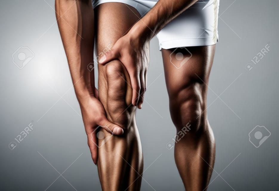 Jeune homme en forme tenant le genou avec les mains dans la douleur après avoir subi une blessure musculaire une entorse ou une crampe à la jambe osseuse cassée pendant l'entraînement en cours d'exécution. Dans Douleurs corporelles et blessures d'entraînement sportif et soins de santé du corps.