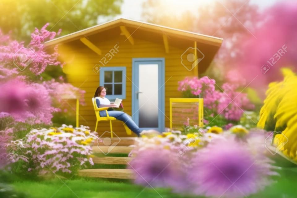 A teenage girl sitting in a chair on the veranda of a garden shed, reading a book. Lots of yellow coneflowers.