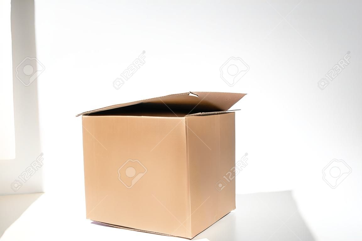 Brown open square corrugated cardboard box on a white background. An empty cardboard box with a shadow from the window. copy space