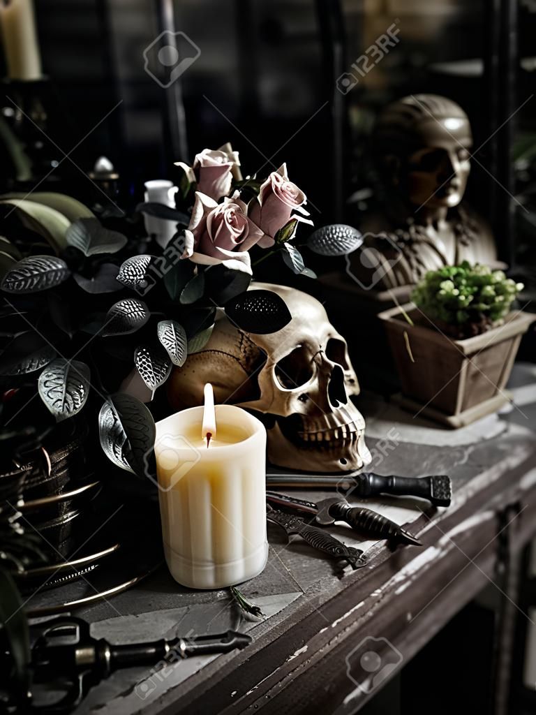 The human skull with white candle light, vintage key chain, bottle, books, flower bouquet in vase and ornamental plants on wooden table in the mystery room
