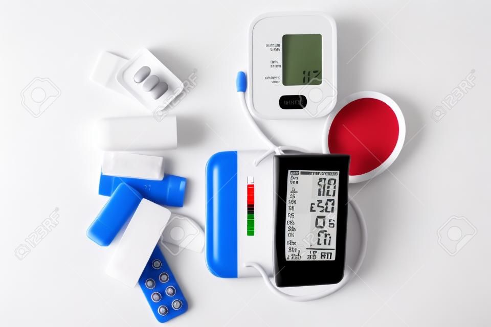 Digital blood pressure monitor and medical pills on white table. Healthcare and medicine concept