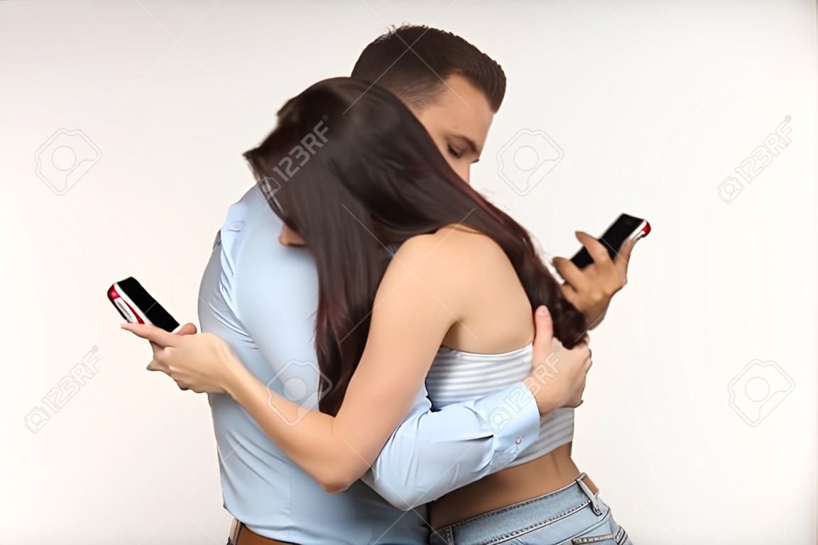 Smartphone addiction concept - young couple hugging and typing on their own phones