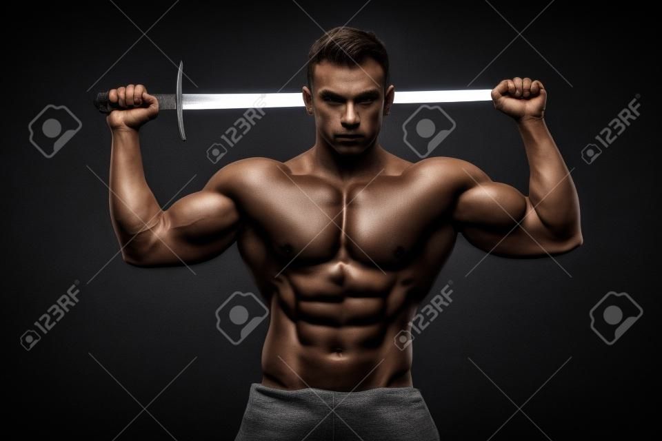 Homem fisiculturista posando com uma espada isolada no fundo preto. Homem sem camisa sério que demonstra seu corpo mascular