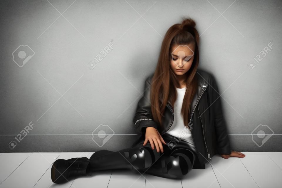 sad girl in a leather jacket rock home sitting on white floor