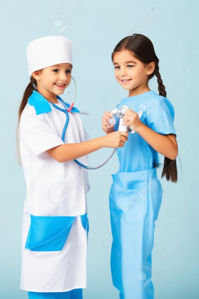 Niña en traje de médico no escucha los pulmones otra chica s, jugando con el estetoscopio, aislado en blanco