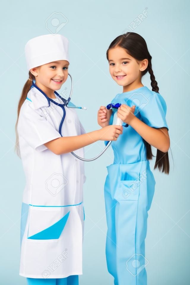 Little girl in doctor costume do listening another girl s lungs, playing with stethoscope, isolated on white